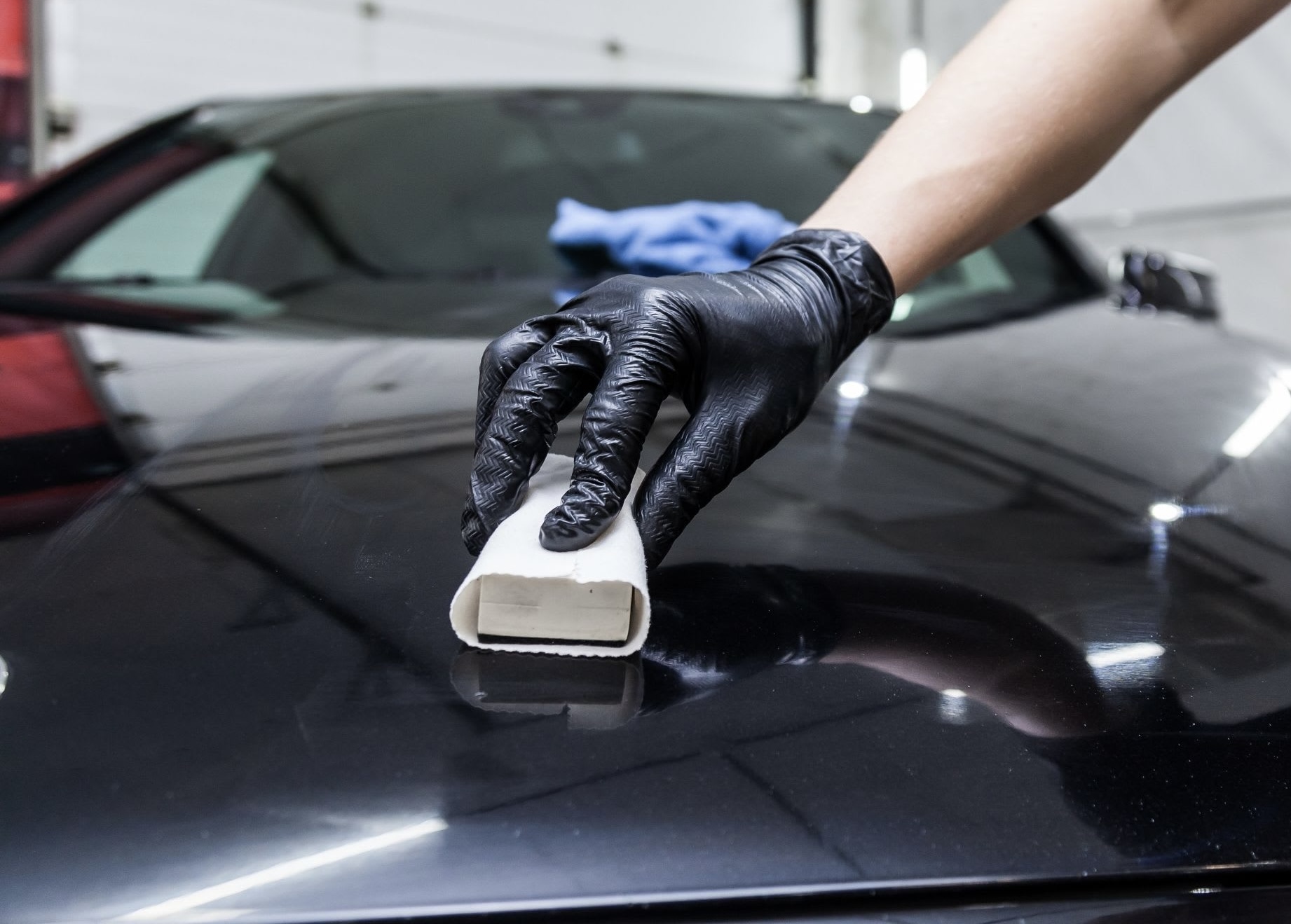 Detailer applying ceramic coating to a vehicle hood by hand with an applicator block