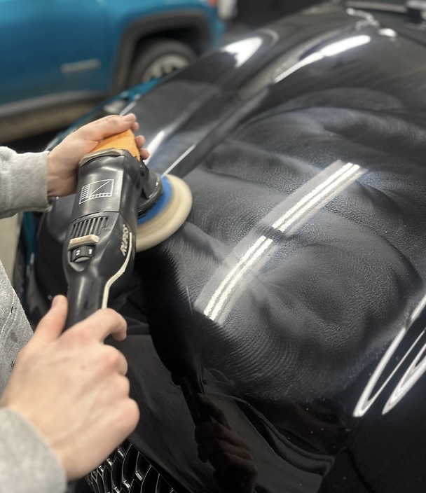 Detailer using a dual-action polisher on a glossy vehicle hood during paint enhancement