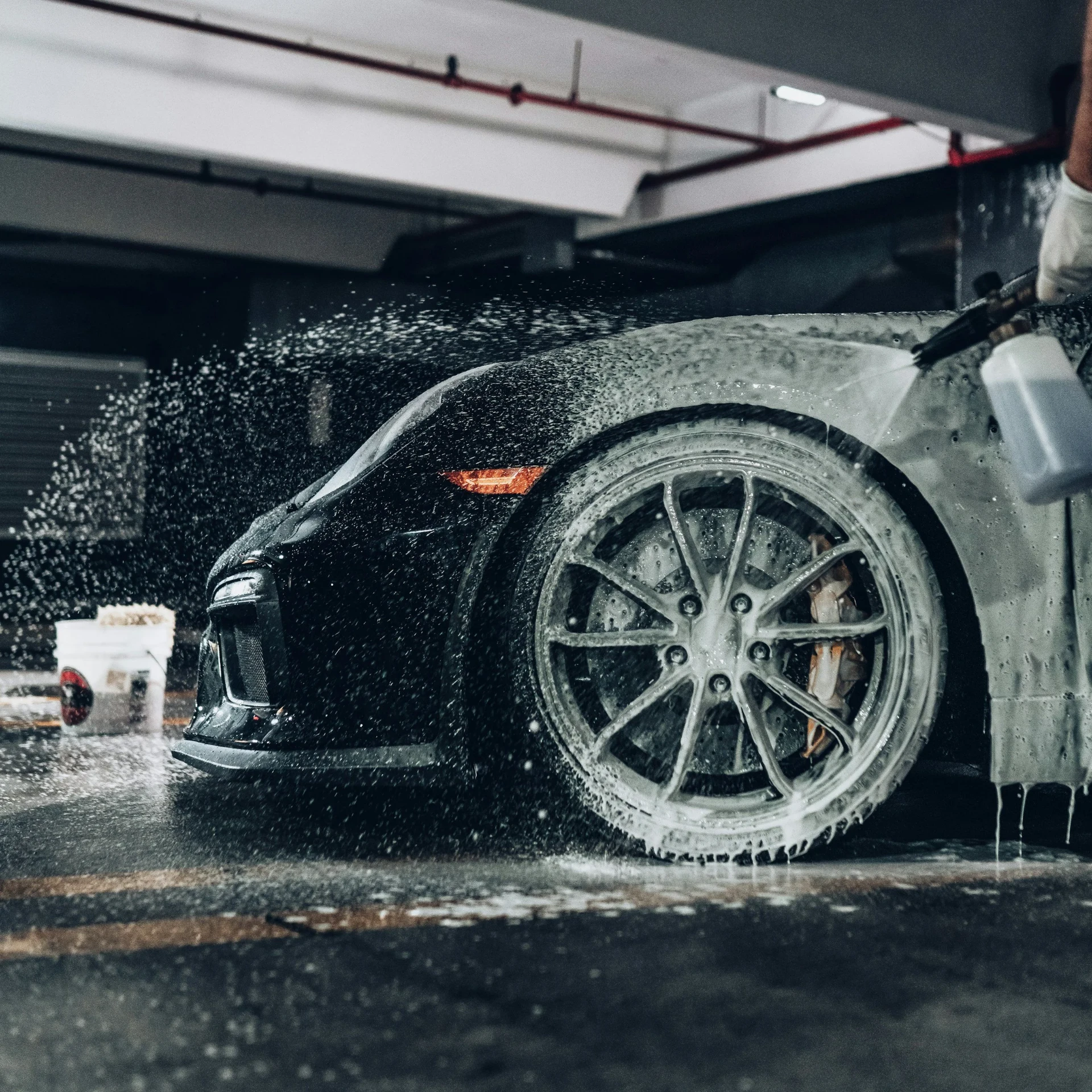 Black sports car covered in cleaning foam during an exterior hand wash